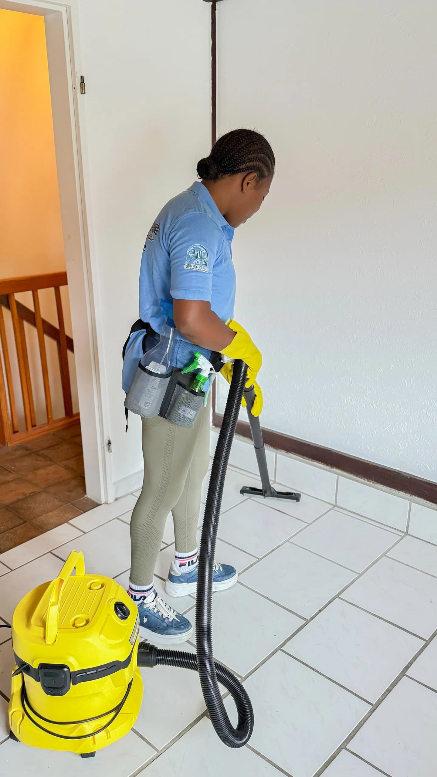 Eine Frau in blauer Kleidung benutzt einen Staubsauger auf einem gefliesten Boden.