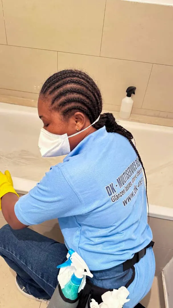 Eine Frau mit Maske und Handschuhen reinigt eine Badewanne.