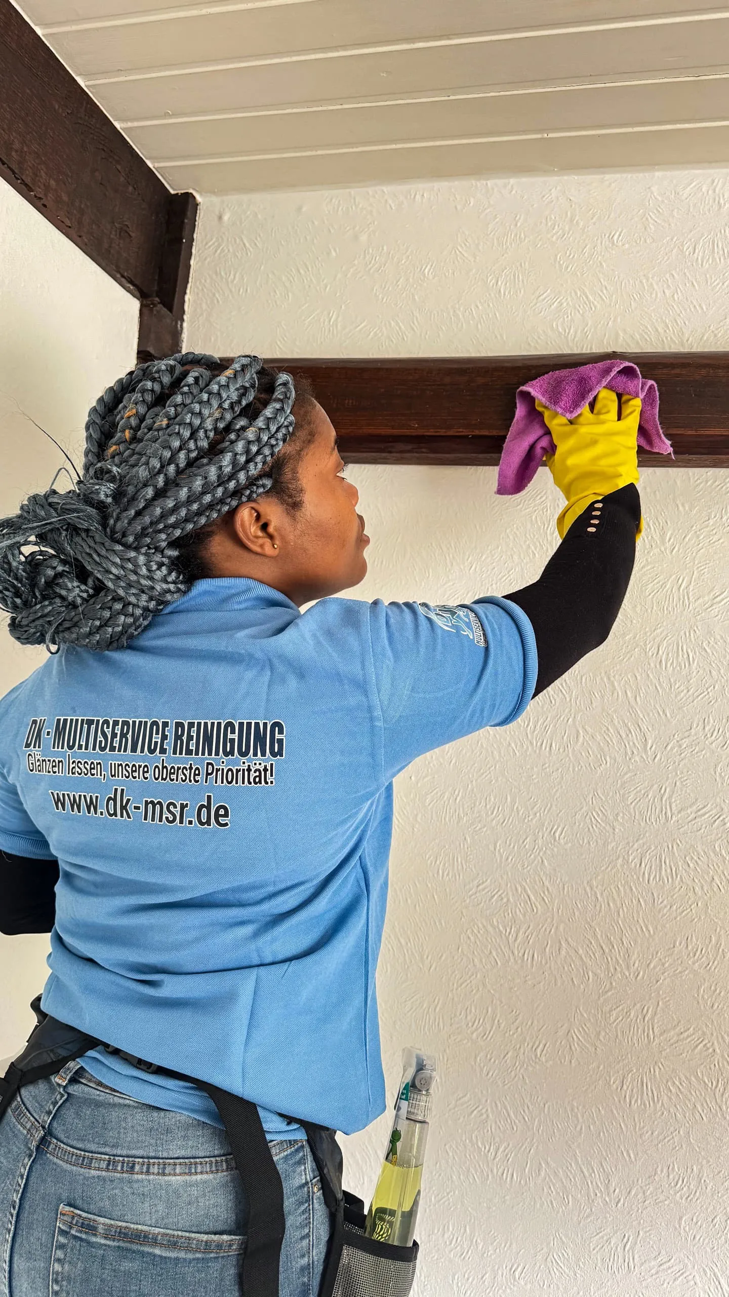 Eine Frau trägt ein blaues Shirt und gelbe Handschuhe, während sie eine Wand putzt.