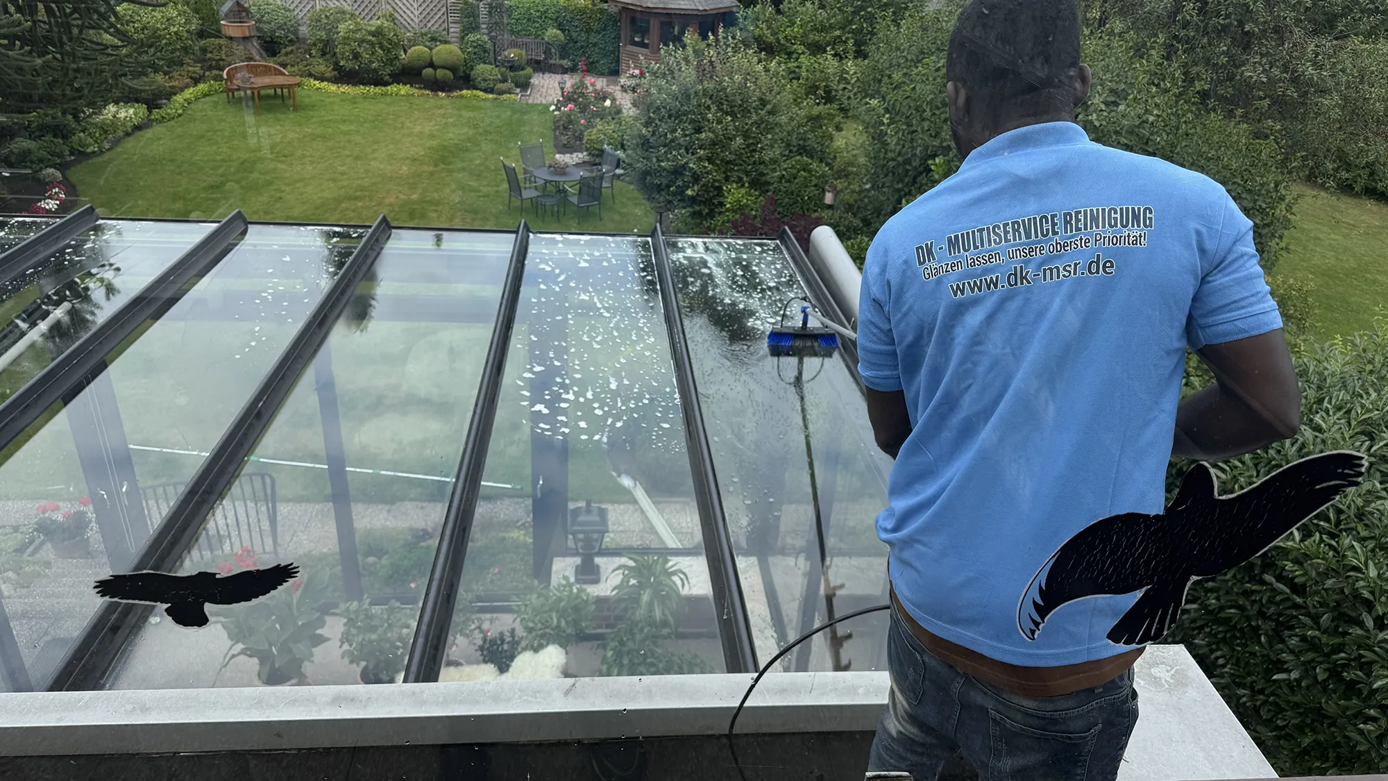 uf dem Dach reinigt ein Mann in einem blauen Shirt das Glas.