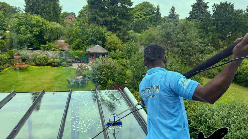 Ein Mann in einem blauen Hemd reinigt das Glas auf einem Dach.